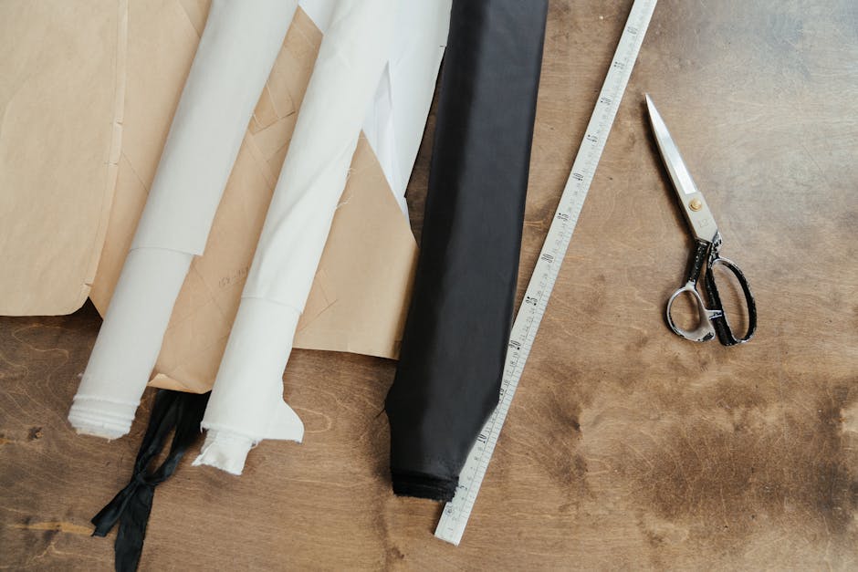 A detailed view of a textile workshop featuring fabric rolls, scissors, and measuring tape on a wooden table.
