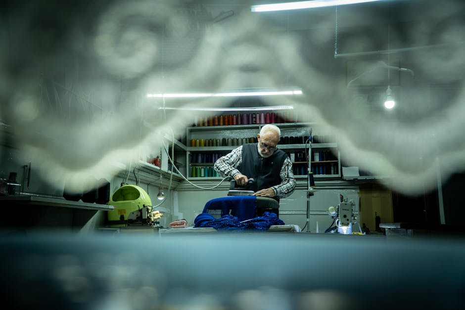 An elderly tailor meticulously working on fabric in a cozy workshop setting.